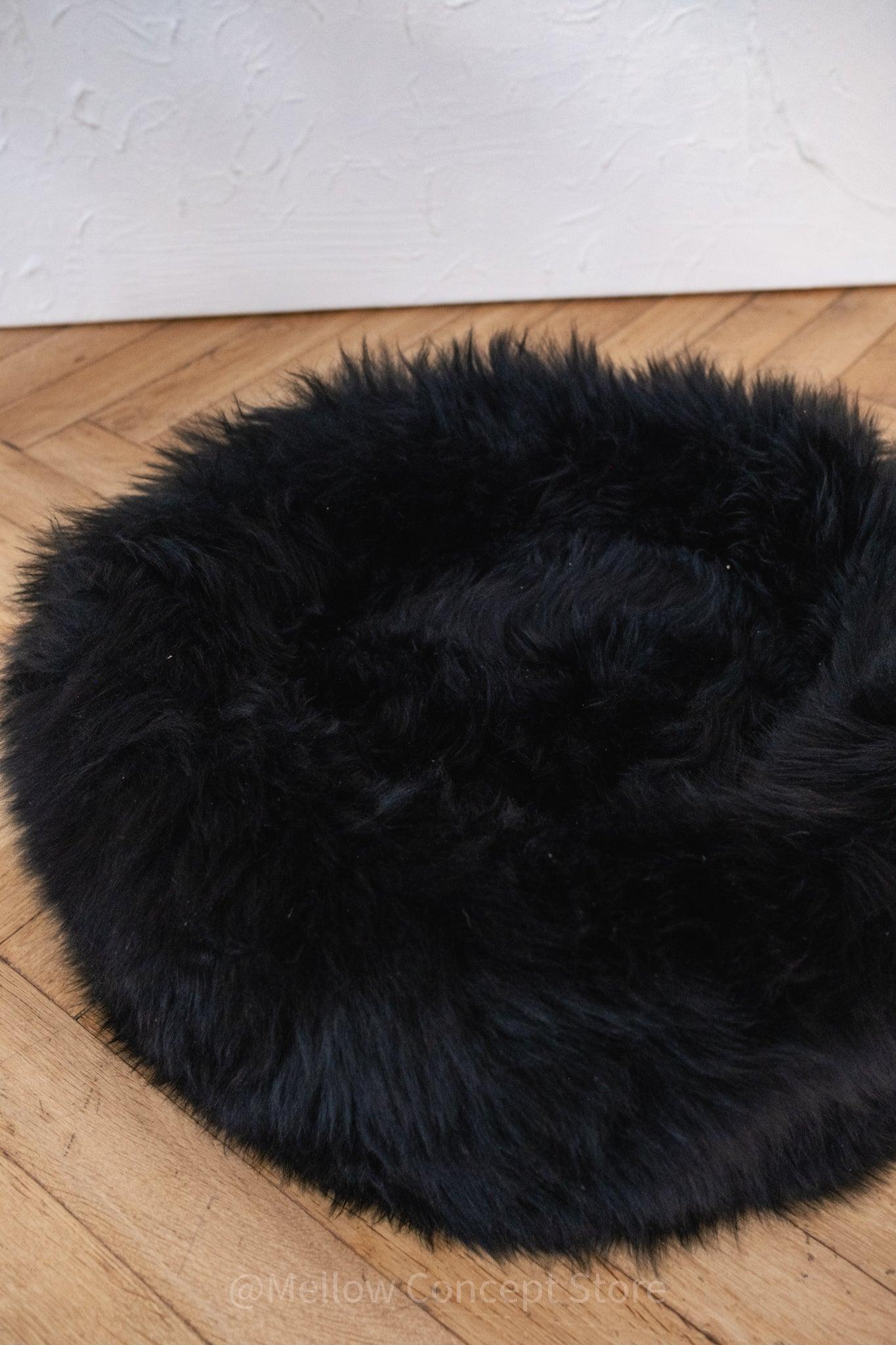 A Round Natural Sheepskin Pet Bed - Black from Mellow Pet Store on a wooden floor.