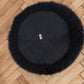 A round black fur rug on a wooden floor made from Mellow Pet Store's Round Natural Sheepskin Pet Bed in Black, creating an eco-friendly and luxurious addition to any room.