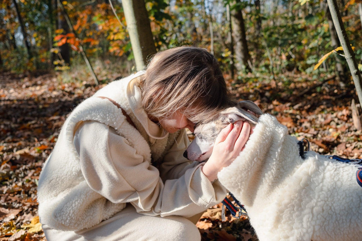 A woman is petting a Woolen Dog Vest - White in the woods from Mellow Pet Store.