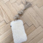 A white Mellow Pet Store sheepskin dog tug toy with a tassel rests on the wooden floor. Crafted from natural sheepskin, this pet accessory exudes luxury and comfort.